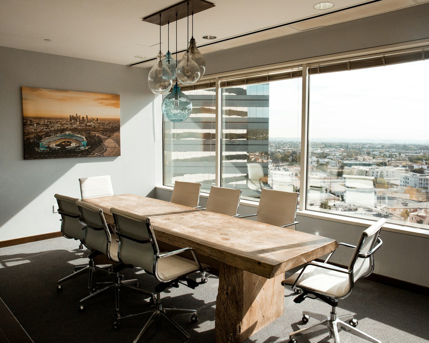 Sala de reuniones con mesa de madera, sillas blancas y vistas a la ciudad